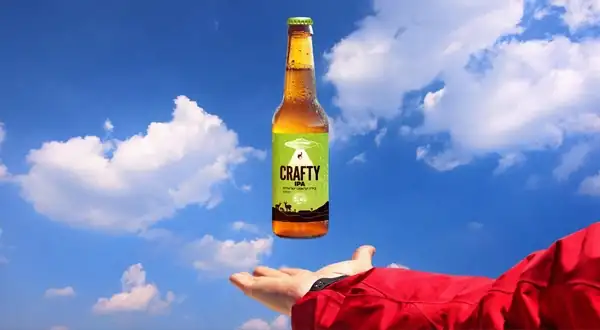 A Crafty bottle floating above a hand in a red sleeve, against drifting clouds