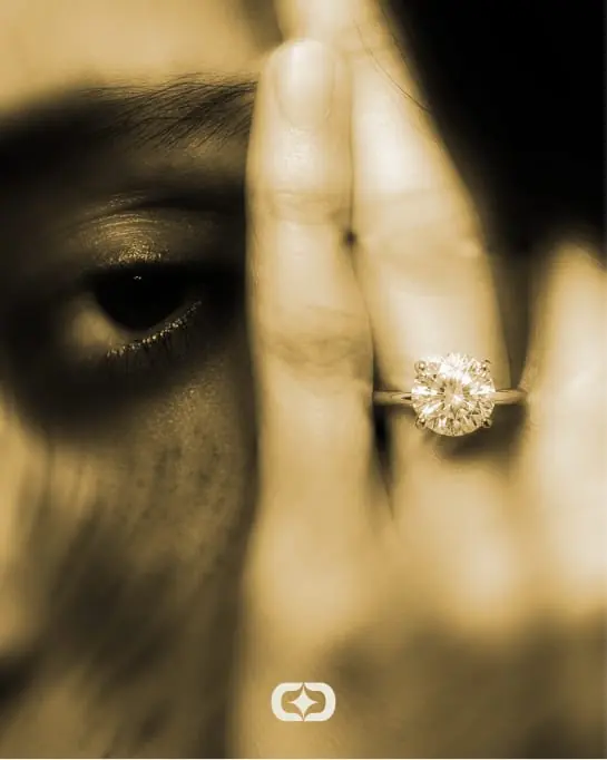 Black-and-white close-up of a hand with a diamond ring across an eye